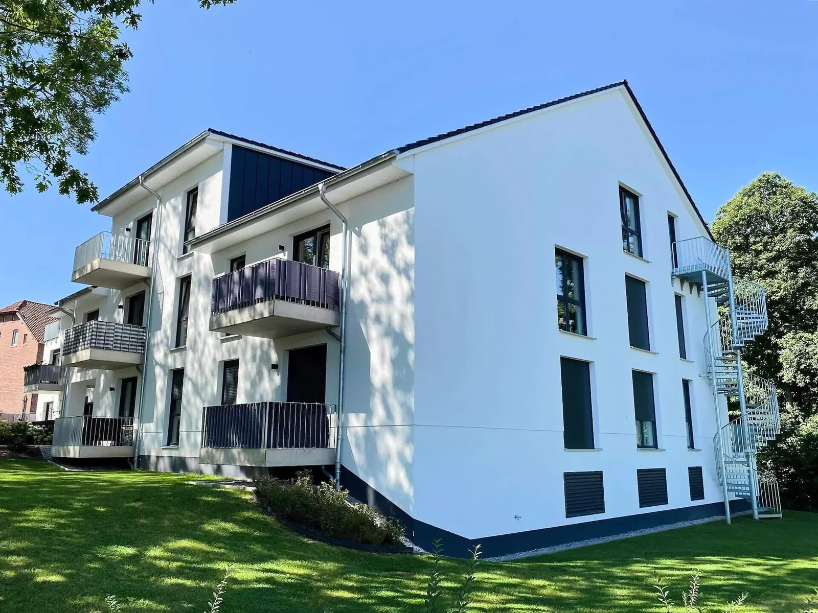 Weißes Mehrfamilienhaus mit Balkonen und Garten