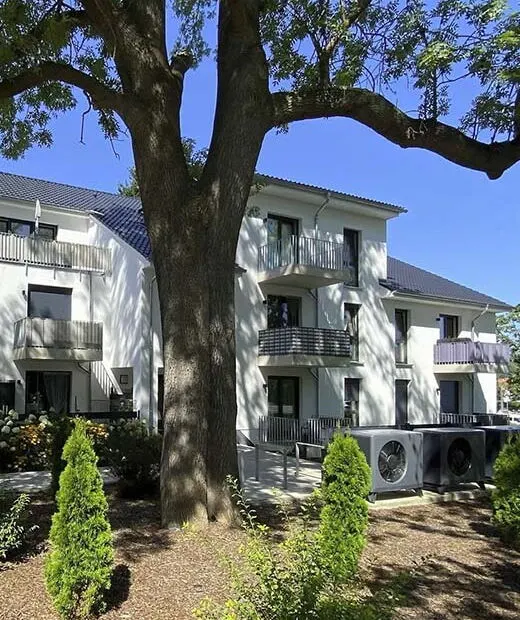 Weißes Mehrfamilienhaus hinter einem großen Baum